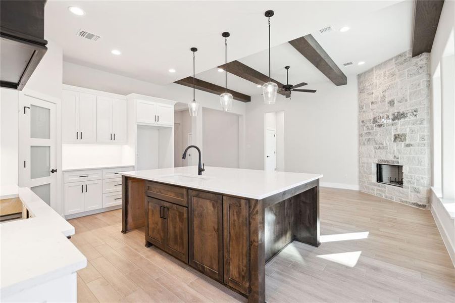 Kitchen with white cabinets, sink, ceiling fan, an island with sink, and beamed ceiling