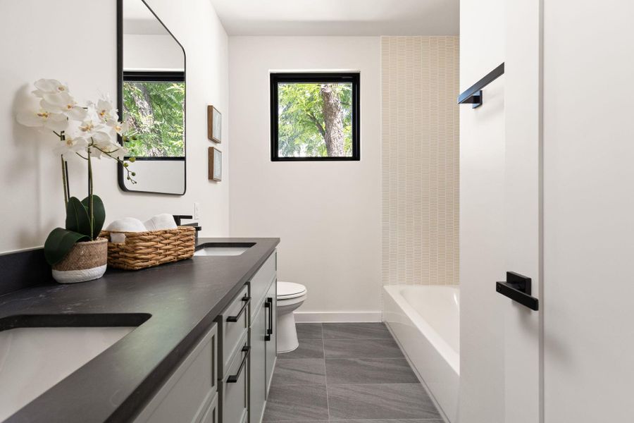 A refined bathroom featuring a sleek double vanity, modern fixtures, and a bright window overlooking green foliage.