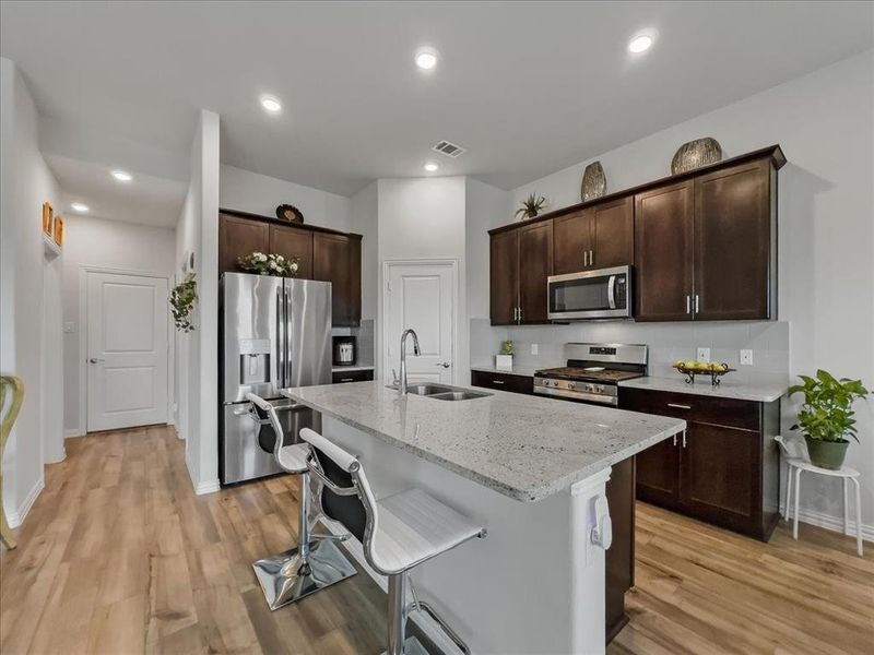 Kitchen featuring stainless steel appliances, light hardwood / wood-style floors, dark brown cabinetry, and breakfast bar