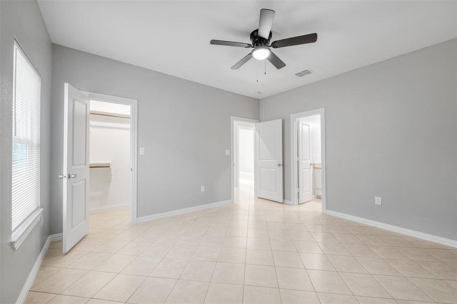 Unfurnished bedroom featuring ensuite bath, ceiling fan, a spacious closet, light tile patterned floors, and a closet