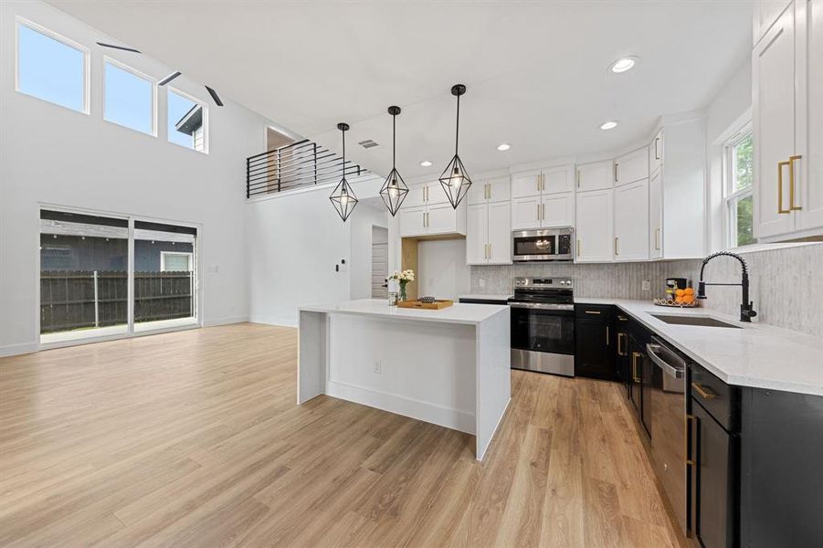 Open concept living space featuring a kitchen island, light wood-style flooring, and high ceilings with large windows Open concept living space featuring a kitchen island, light wood-style flooring, and high ceilings with large windows