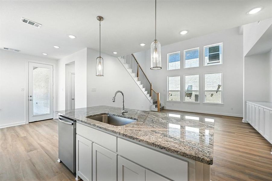 Kitchen featuring a kitchen island with sink, light stone counters, white cabinetry, light wood finished floors, and pendant lighting Kitchen featuring a kitchen island with sink, light stone counters, white cabinetry, light wood finished floors, and pendant lighting