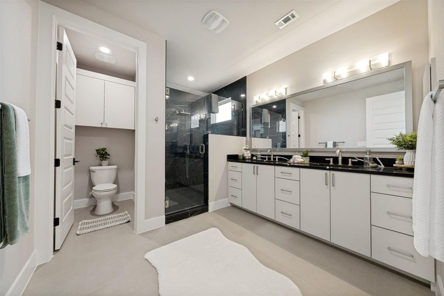 A sleek, contemporary primary bath features a dual vanity and an enclosed shower with dark tile accents. A sleek, contemporary primary bath features a dual vanity and an enclosed shower with dark tile accents.