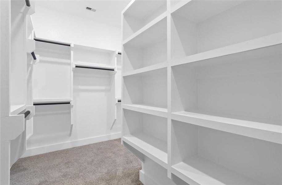 The spacious walk-in closet is equipped with clean white shelving and sturdy matte black hanging rods, offering extensive solutions for organizing an entire wardrobe.