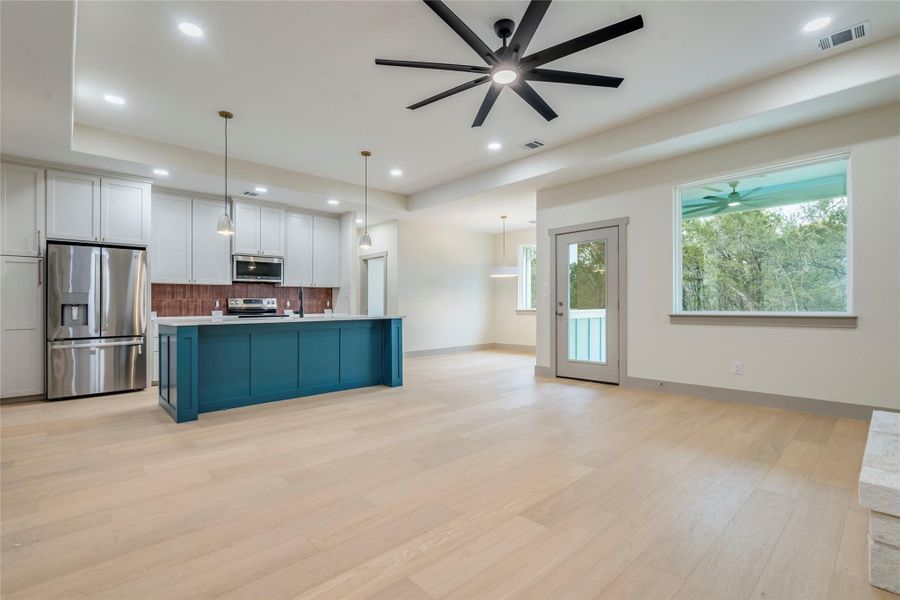 Kitchen featuring open floor plan, stainless steel appliances, white cabinets, an island with sink, and a tray ceiling