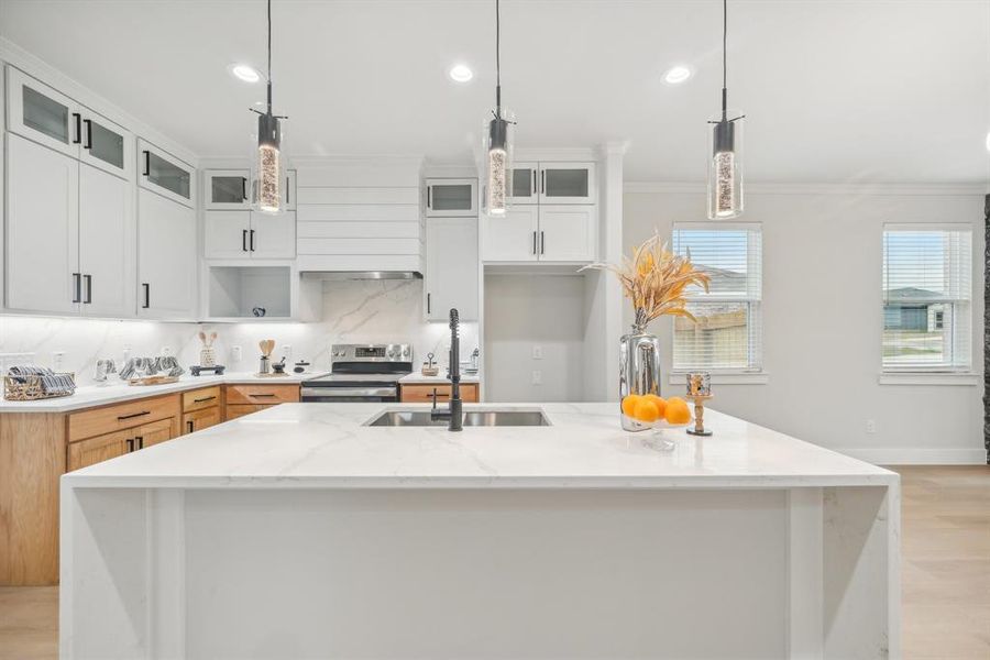 Kitchen featuring white cabinets, decorative light fixtures, electric range, light stone counters, and a kitchen island with sink