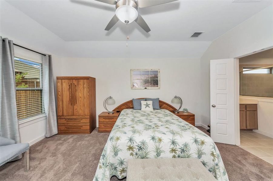 Bedroom featuring ensuite bathroom, ceiling fan, vaulted ceiling, and light colored carpet