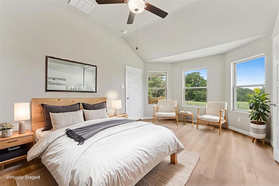 A tranquil primary bedroom features high ceilings, a cooling ceiling fan, and ample natural light from multiple windows.