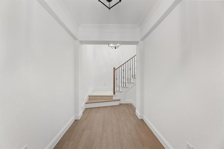 Hallway with light wood-style flooring, stairway, crown molding, and a chandelier Hallway with light wood-style flooring, stairway, crown molding, and a chandelier