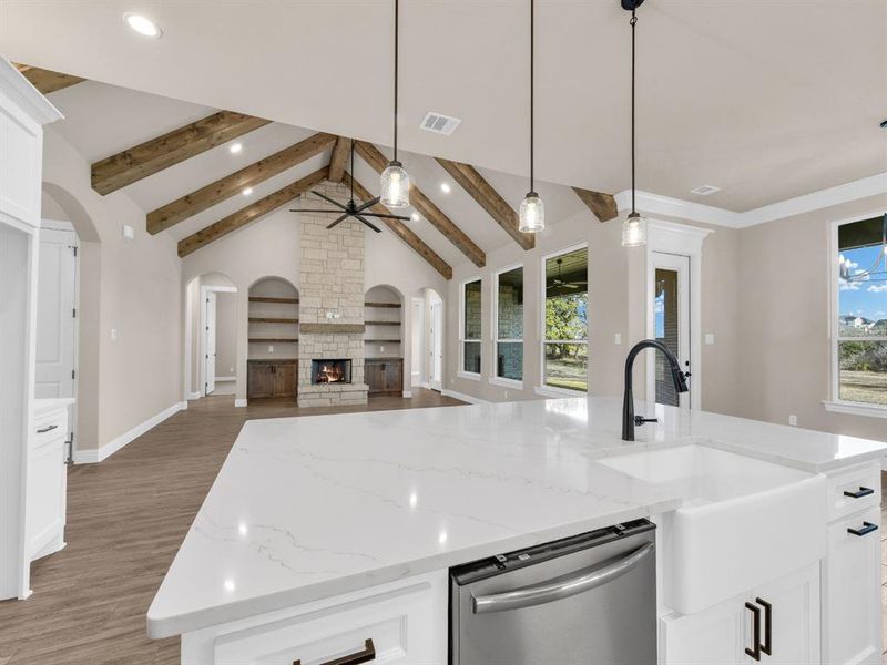 Kitchen featuring vaulted ceiling with beams, stainless steel dishwasher, dark hardwood / wood-style floors, an island with sink, and decorative light fixtures