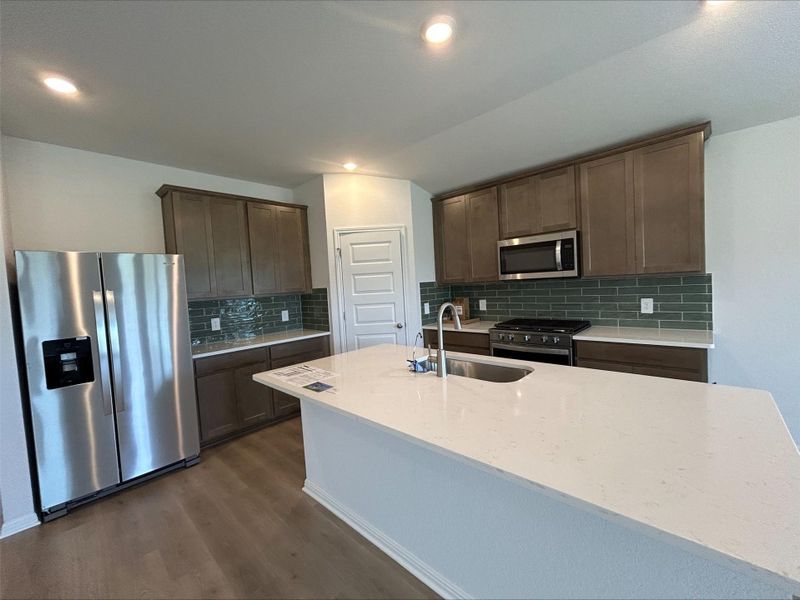 Kitchen with stainless steel appliances, backsplash, dark brown cabinetry, light stone countertops, and dark wood finished floors