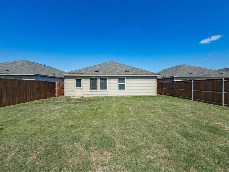 Expansive backyard featuring a manicured lawn, full wood fencing, and a rear exterior door