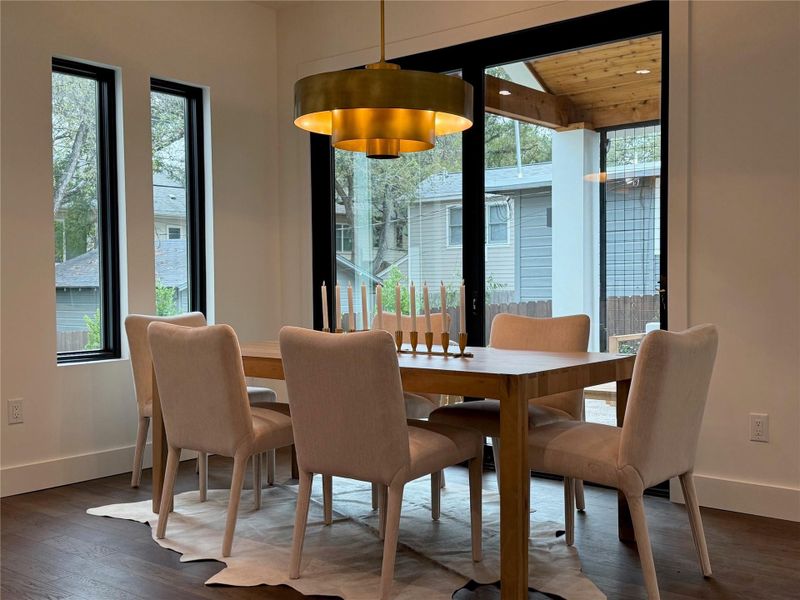 Dining area featuring a prominent gold-toned drum pendant light fixture, dark wood-finish flooring, and white baseboards