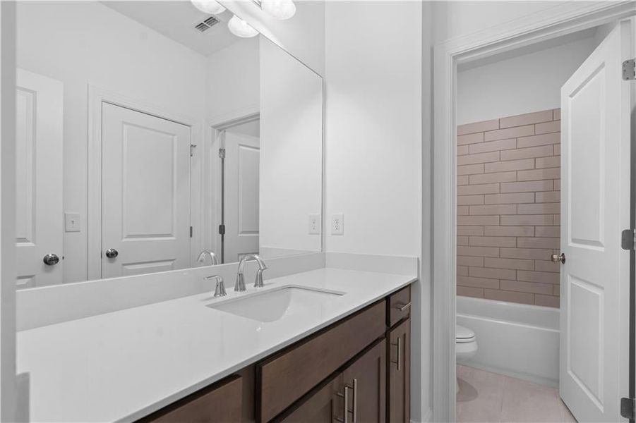 This well-appointed shared bathroom features a sleek vanity with ample storage and counter space, ideal for everyday convenience. The tub is accented by a classic tile surround, offering both style and durability. Designed for comfort and functionality,