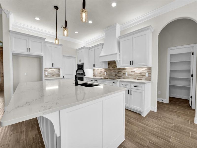 Kitchen with custom range hood, ornamental molding, a sink, light stone countertops, and wood tiled floor Kitchen with custom range hood, ornamental molding, a sink, light stone countertops, and wood tiled floor