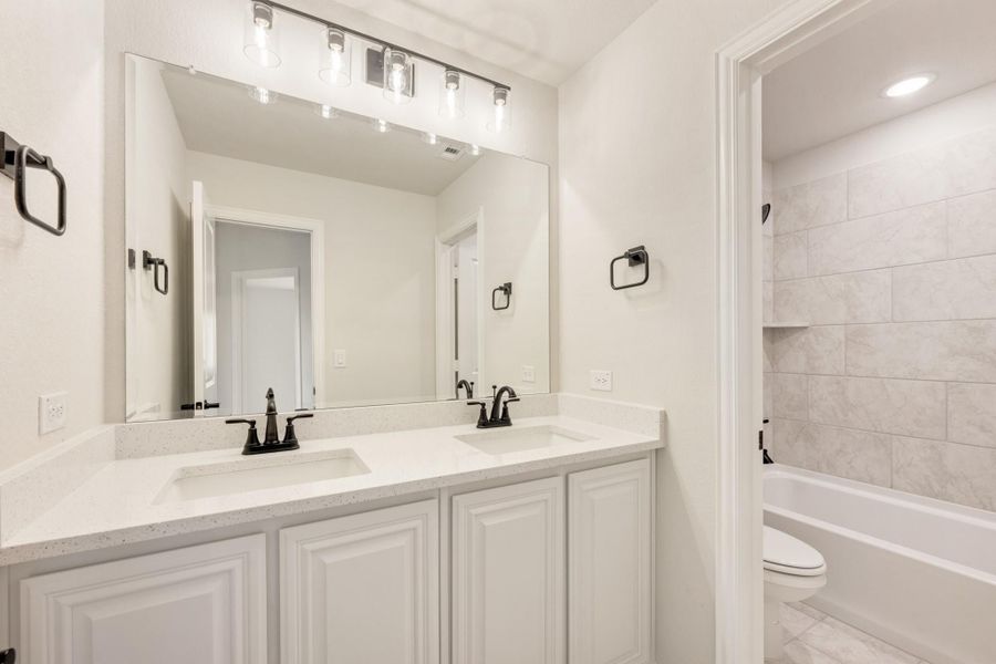 Bathroom with double sink vanity, white cabinets, large mirror, and tiled tub-shower combo