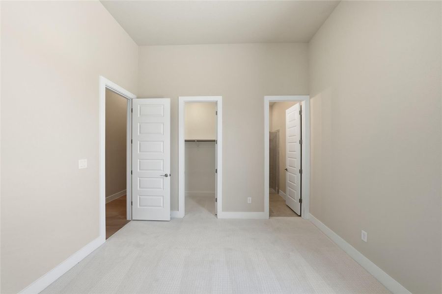Unfurnished bedroom with light colored carpet, a spacious closet, and connected bathroom