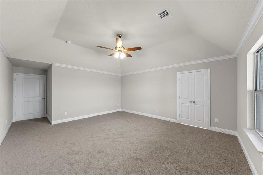 Spacious room featuring vaulted ceilings, crown molding, a ceiling fan with integrated lighting, neutral wall tones, and carpet flooring
