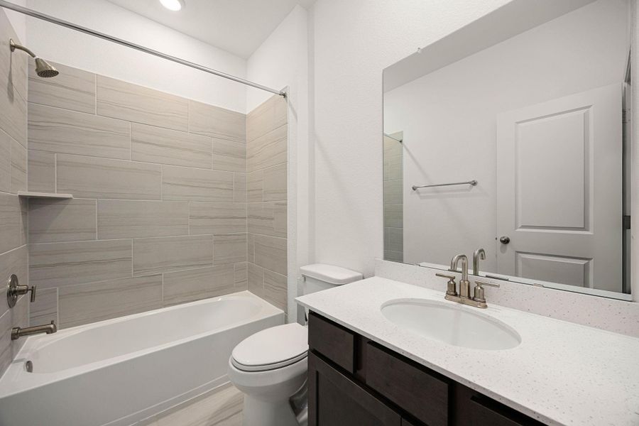 Modern bathroom featuring a sleek vanity with a quartz countertop, a large mirror, and a stylish tiled shower and bathtub combo.