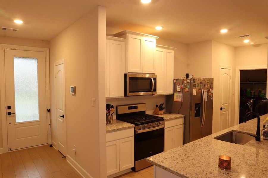 Kitchen featuring stainless steel appliances, white cabinets, light stone countertops, recessed lighting, and light wood finished floors Kitchen featuring stainless steel appliances, white cabinets, light stone countertops, recessed lighting, and light wood finished floors