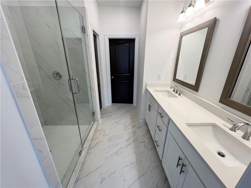 Owners Bathroom featuring marble finish floors, double vanity, and a stall shower
