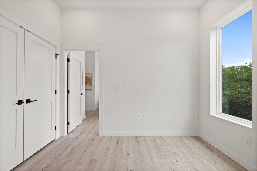 This bright room features light-colored flooring, white walls, and a window offering views of green trees and the sky