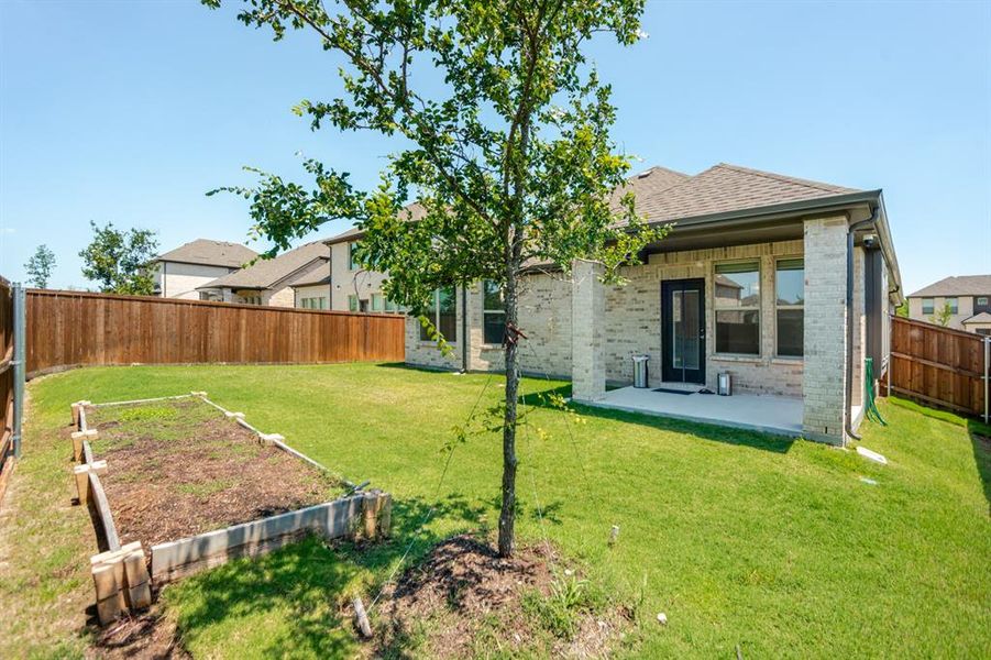 Expansive backyard featuring a covered patio, a manicured lawn, a raised garden bed, and a privacy fence