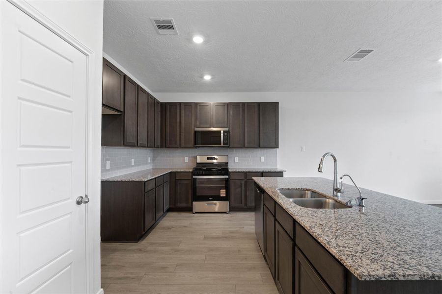 The kitchen features high ceilings, stained wood cabinets, granite countertops, SS appliances including microwave, modern tile backsplash, recessed lighting, and a pantry all overlooking your huge Great Room.