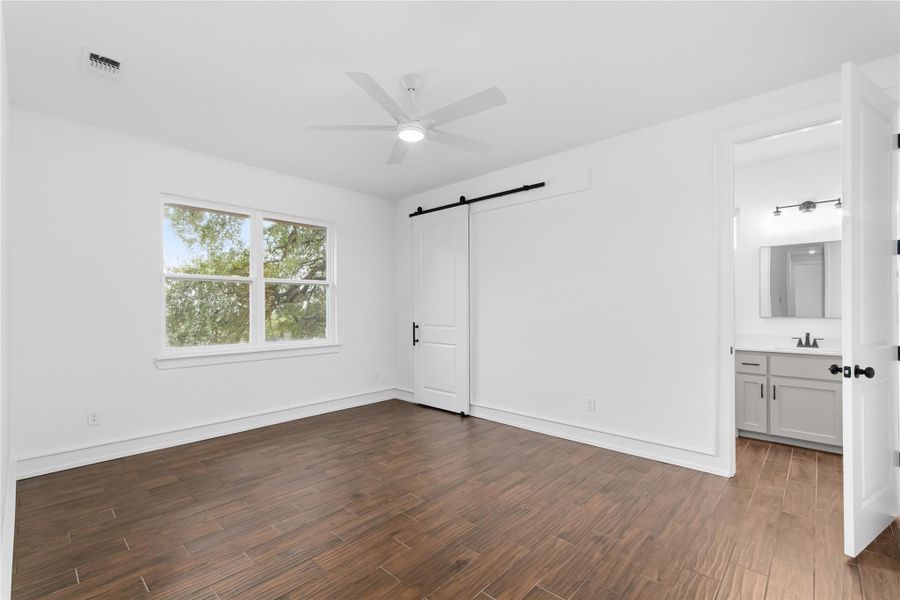 Unfurnished bedroom featuring a barn door, dark wood-style floors, a sink, baseboards, and ensuite bathroom Unfurnished bedroom featuring a barn door, dark wood-style floors, a sink, baseboards, and ensuite bathroom
