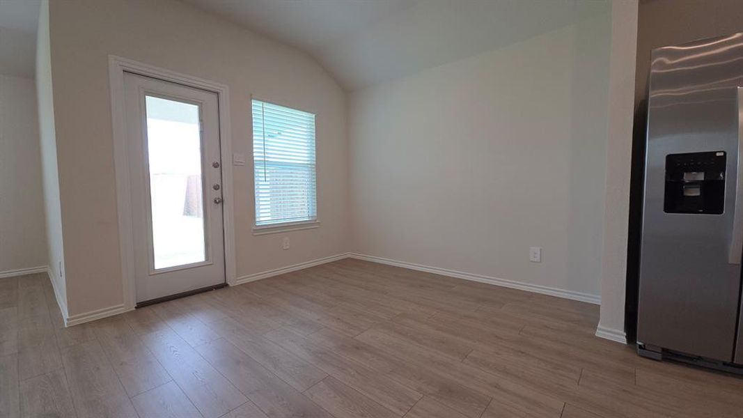 Open-concept living area with wood-finish flooring, a full-lite exterior door, and a stainless steel refrigerator