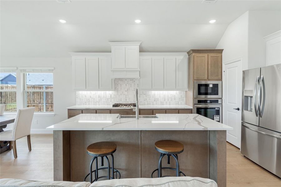 Kitchen with large island, quartz countertops, white cabinets, tile backsplash, and stainless steel appliances