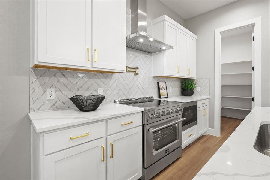 Kitchen featuring white cabinets, high end stainless steel range, light stone countertops, and wall chimney exhaust hood