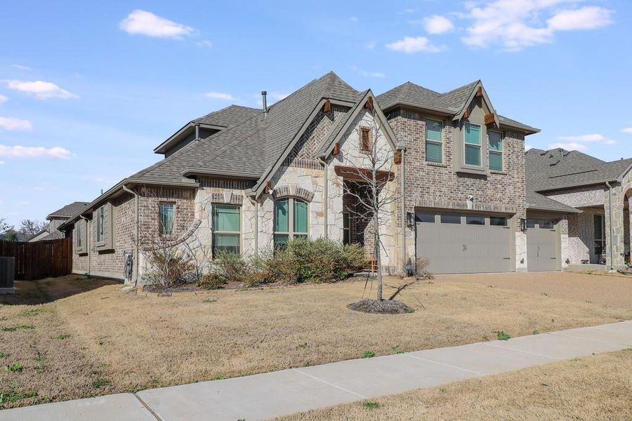 View of front of property featuring an attached garage, brick siding, stone siding, roof with shingles, and a front lawn View of front of property featuring an attached garage, brick siding, stone siding, roof with shingles, and a front lawn