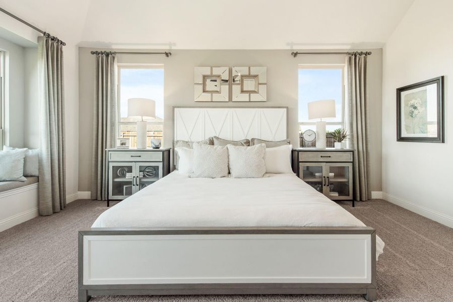 Master bedroom with white upholstered headboard, matching nightstands, gray carpet, and two windows with gray curtains