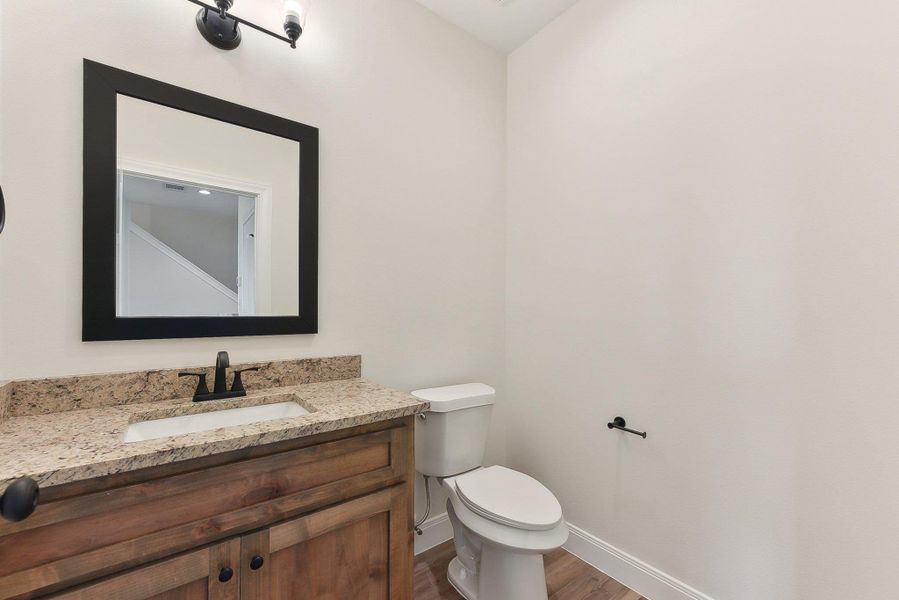 Half Bathroom featuring wood finished floors, vanity, toilet, and baseboards