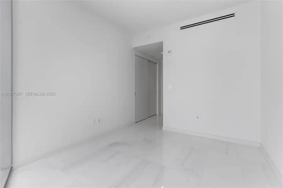 Minimalist interior space featuring polished light-toned stone flooring and dual-panel sliding closet doors