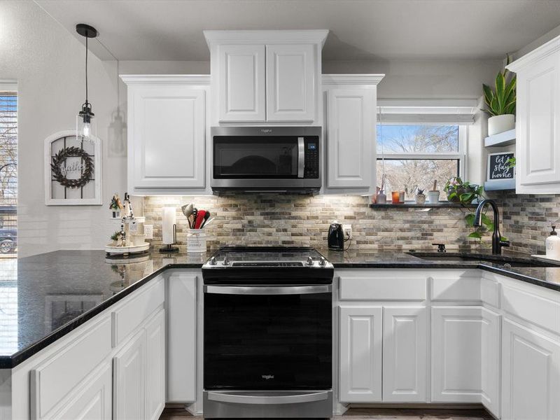 Kitchen with a sink, decorative backsplash, stainless steel appliances, white cabinets, and decorative light fixtures