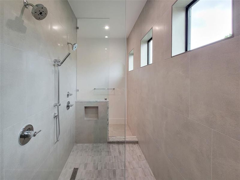 Primary shower with double Delta shower heads & controls, built in product holder and custom tile flooring.