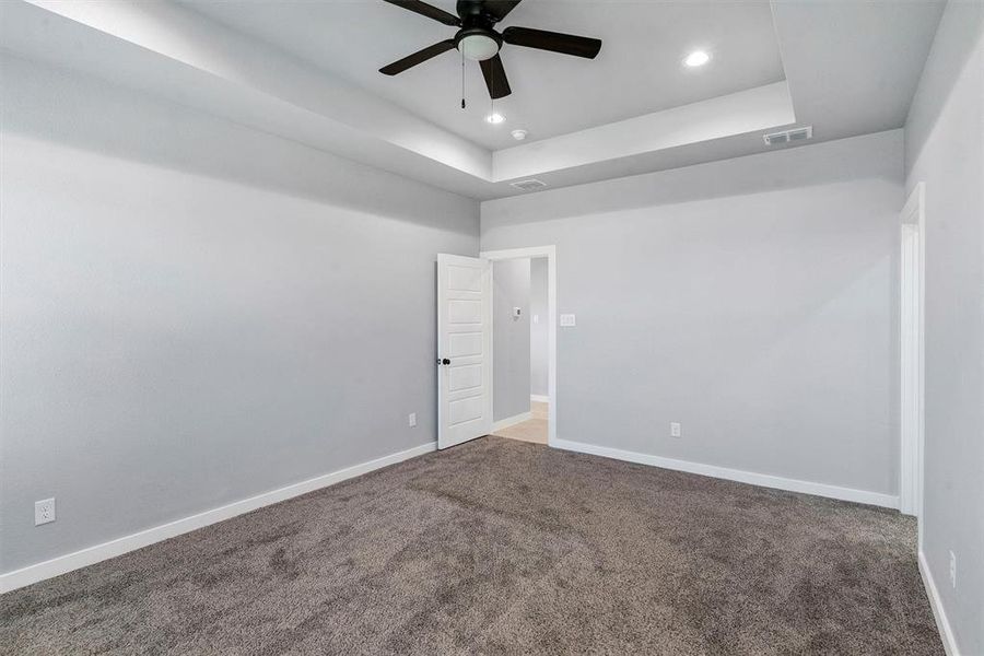 Carpeted empty room featuring ceiling fan and a raised ceiling