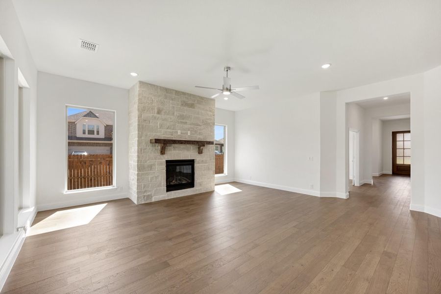 Open living room with stone fireplace, wood mantel, hardwood floors, and ceiling fan
