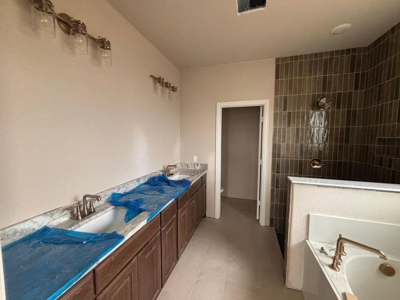 Dual vanity with wood-finish cabinetry and light-toned countertops, featuring two undermount sinks and brushed bronze fixtures