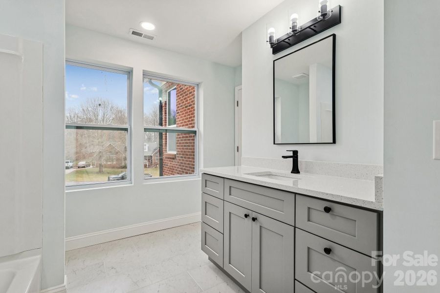 Gorgeous Jack and Jill Bathroom with quartz counter top, tile flooring, elegant lighting, framed mirror and large windows for natural lighting
