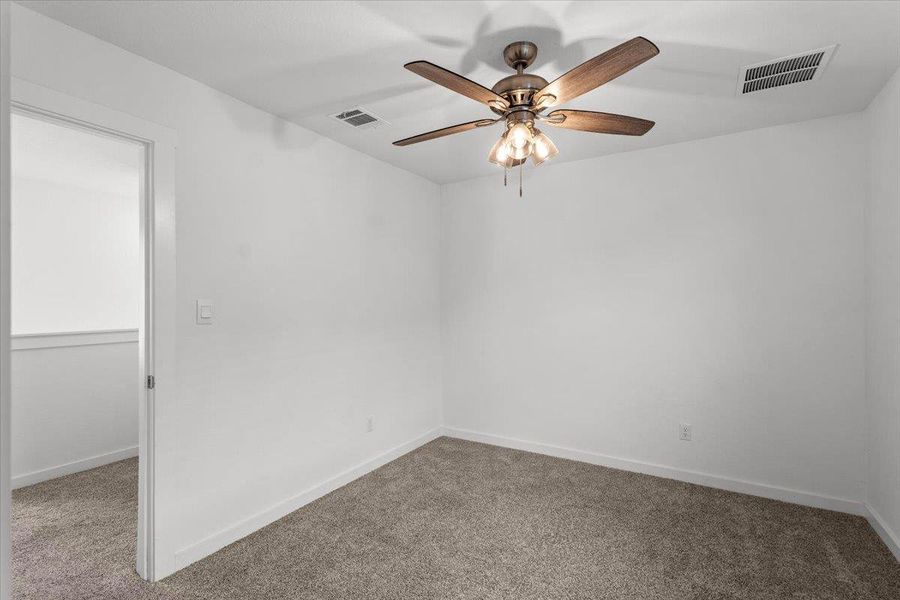 A well-lit room with neutral walls and soft carpeting features a convenient ceiling fan.