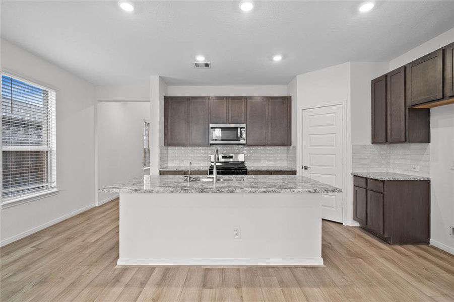 This spacious kitchen features high ceilings, stained wood cabinets, granite countertops, SS appliances, modern tile backsplash, recessed lighting, huge granite kitchen island with large single sink and space for breakfast bar, and a pantry all overlooking your huge family room.