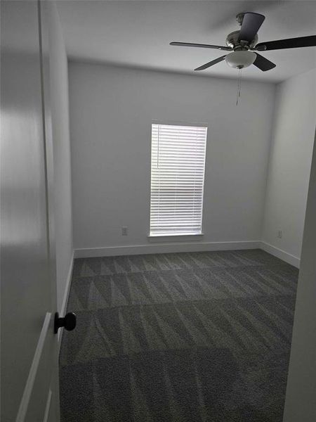 Empty room featuring dark colored carpet and ceiling fan