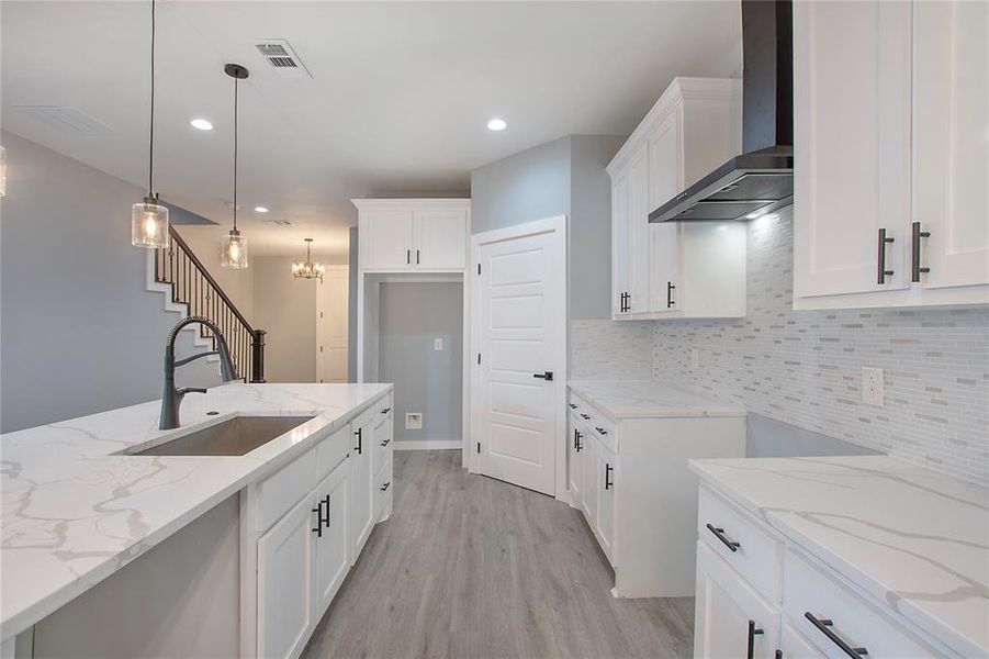 Kitchen with sink, light stone countertops, wall chimney range hood, and white cabinetry