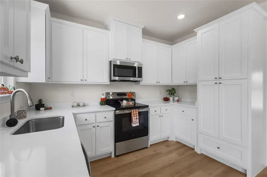 Kitchen with stainless steel appliances, light wood finished floors, white cabinets, recessed lighting, and light stone counters