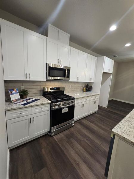 Kitchen with white cabinets, dark wood-type flooring, and gas stove