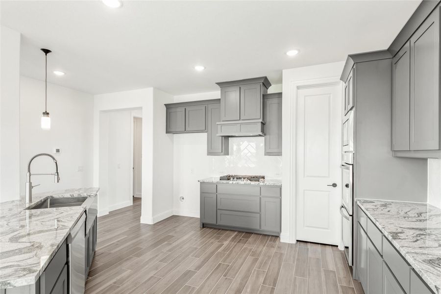Kitchen with gray shaker cabinets, marble countertops, wood-look tile floors, and a built-in range hood Kitchen with gray shaker cabinets, marble countertops, wood-look tile floors, and a built-in range hood