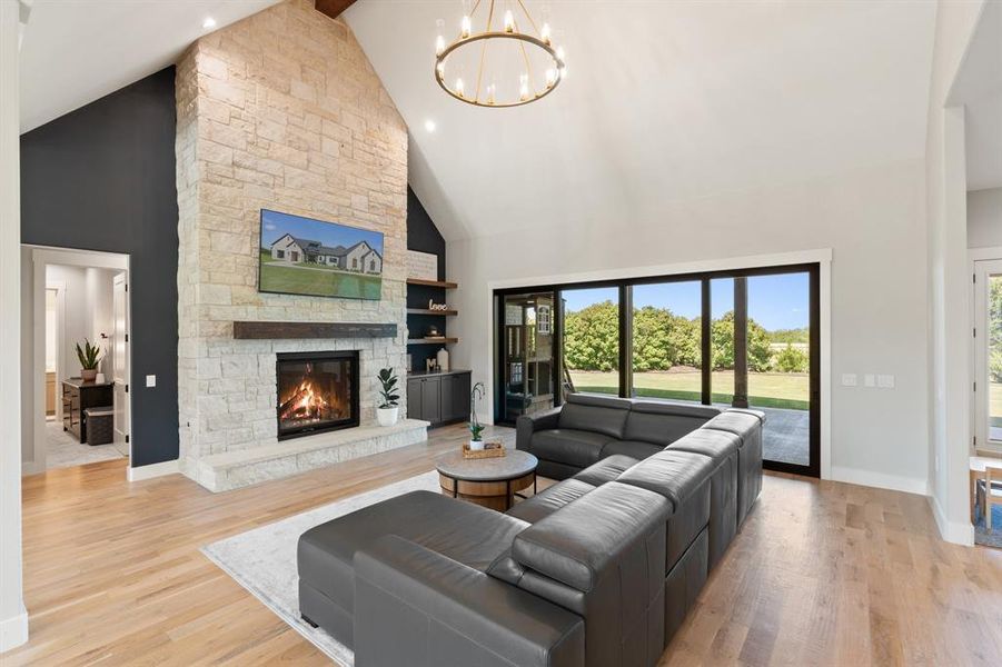 Living room featuring high vaulted ceiling, light hardwood / wood-style flooring, a stone fireplace, and an inviting chandelier